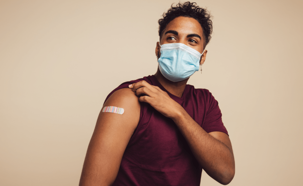 Young man wearing a mask while lifting up his sleeve to show off his band-aid reflecting his recent vaccination.